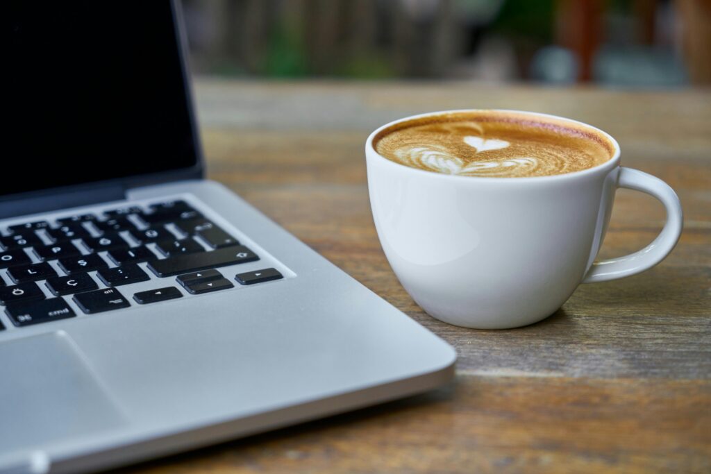 pexels-photo-414628-414628 Close-up of a latte coffee with heart art next to a laptop on a rustic wooden table.